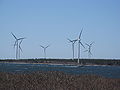 Seven three-blade wind turbines on the shore. A fishing boat is passing by. 